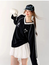 Person wearing a black tracksuit with white accents and a white skirt, holding boxing gloves.